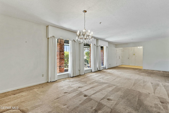 spare room with a textured ceiling, carpet, baseboards, and an inviting chandelier