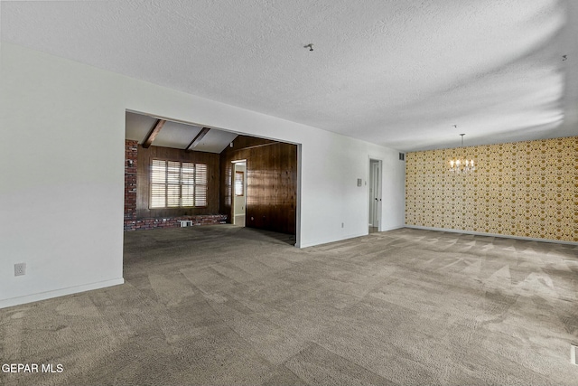 unfurnished living room with a textured ceiling, carpet flooring, baseboards, vaulted ceiling, and an inviting chandelier