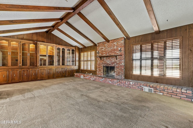 unfurnished living room featuring lofted ceiling with beams, wood walls, a fireplace, carpet flooring, and visible vents