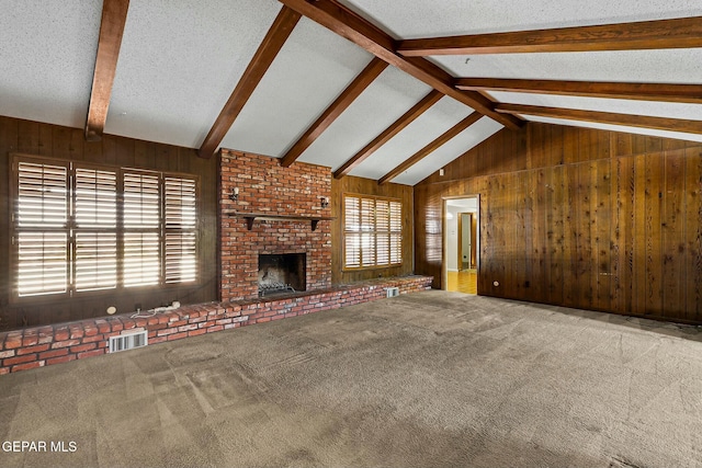 unfurnished living room with a healthy amount of sunlight, wooden walls, a fireplace, and carpet flooring