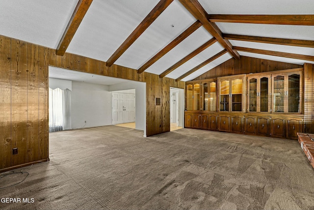 unfurnished living room featuring carpet flooring, wood walls, and lofted ceiling with beams