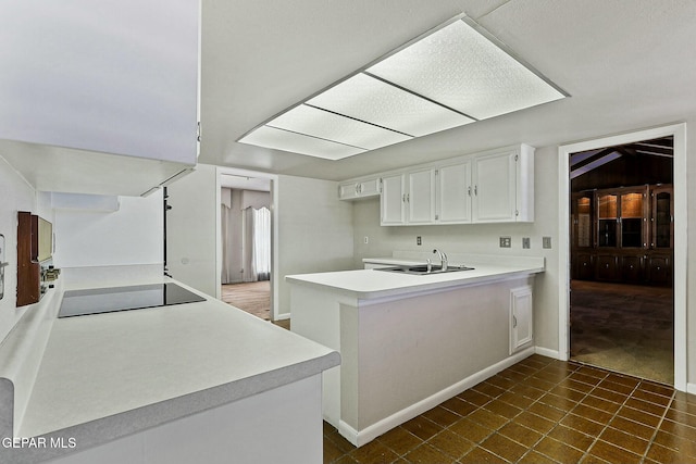 kitchen with black electric stovetop, light countertops, white cabinets, a sink, and a peninsula