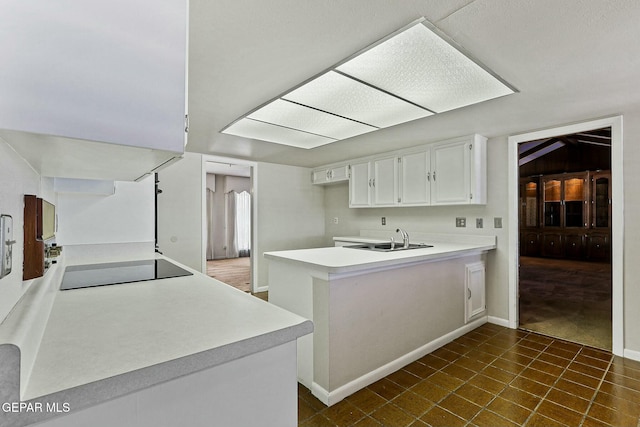 kitchen with black electric stovetop, a peninsula, a sink, white cabinets, and light countertops