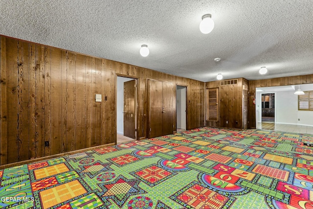 unfurnished bedroom with light colored carpet, visible vents, wood walls, and a textured ceiling