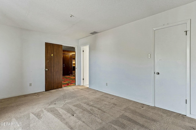 carpeted empty room with baseboards, visible vents, and a textured ceiling