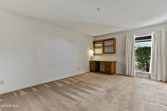 unfurnished room with a textured ceiling, built in desk, visible vents, and light colored carpet