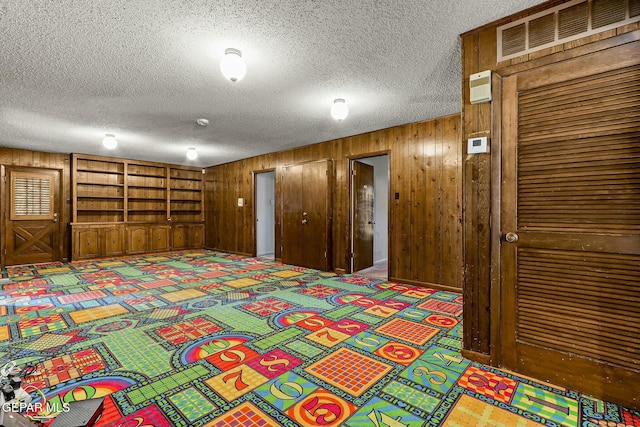 unfurnished bedroom with a textured ceiling, wood walls, a closet, and visible vents