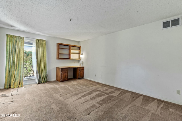 unfurnished room with light carpet, baseboards, visible vents, a textured ceiling, and built in desk