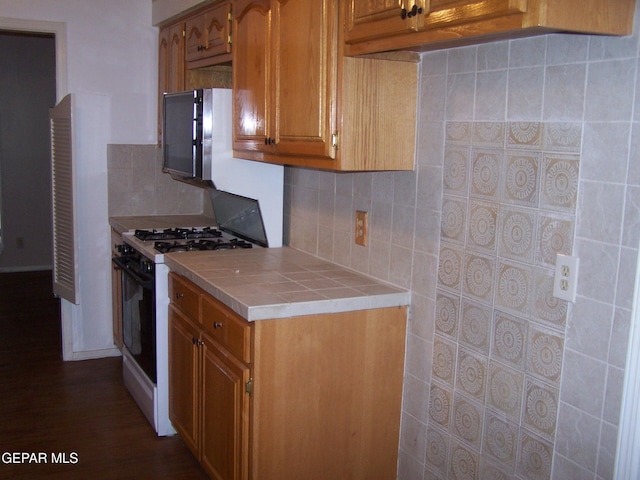 kitchen featuring decorative backsplash, tile counters, white gas range, and brown cabinets