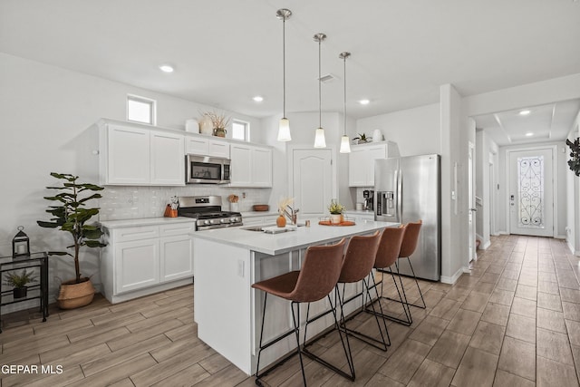 kitchen featuring a center island with sink, appliances with stainless steel finishes, decorative backsplash, and light countertops