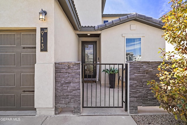 entrance to property with a garage, stone siding, a tile roof, and stucco siding