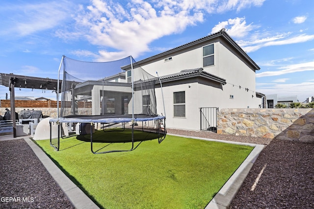 back of property featuring a yard, a trampoline, a tile roof, and stucco siding