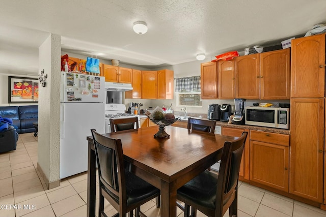 160 Indian Head Rd, Tornillo, TX 79853 - kitchen with light tile patterned floors, a textured ceiling, under cabinet range hood, white appliances, and brown cabinetry