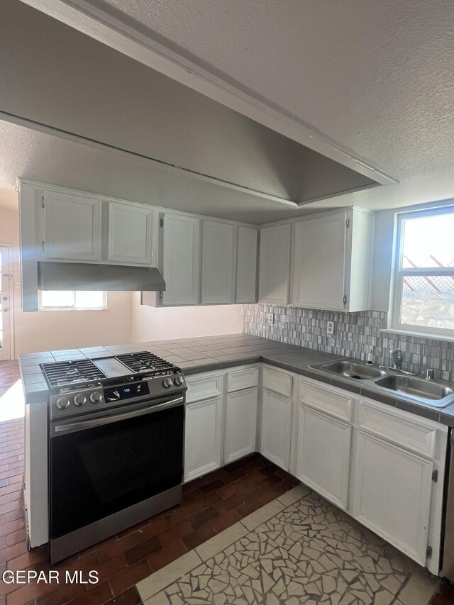 kitchen featuring a textured ceiling, gas range, a sink, white cabinets, and tile counters