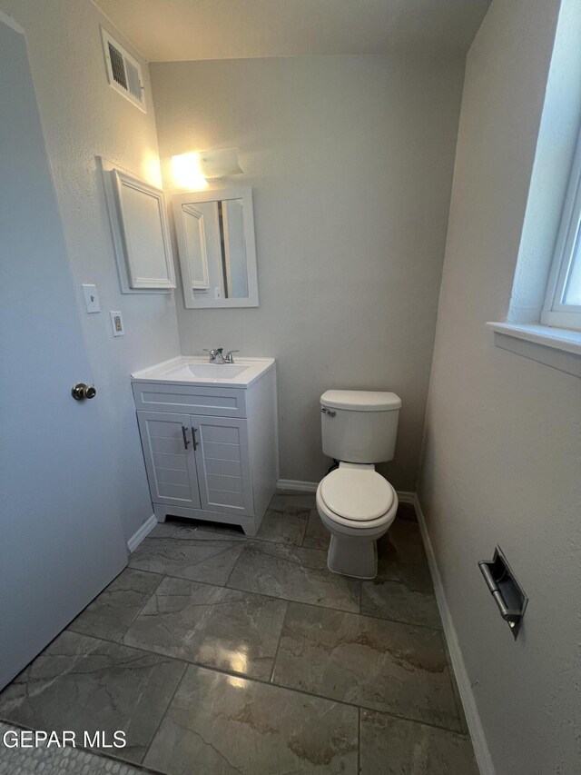 half bath with vanity, toilet, marble finish floor, baseboards, and visible vents