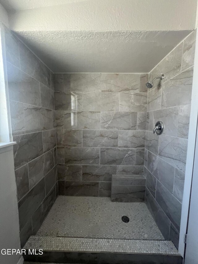 bathroom with a textured ceiling and tiled shower