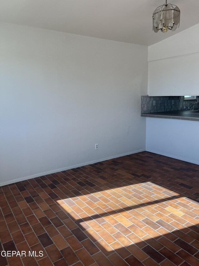 interior space featuring an inviting chandelier, baseboards, and brick floor