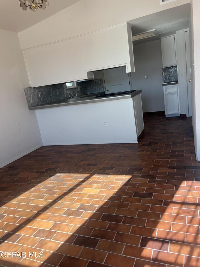 kitchen featuring brick floor, dark countertops, and tasteful backsplash