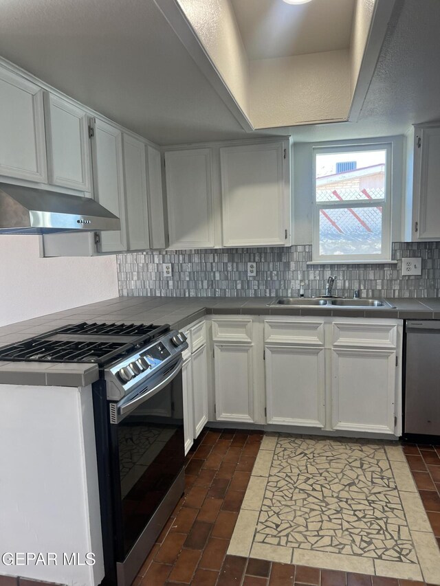 kitchen with a sink, appliances with stainless steel finishes, tile counters, and under cabinet range hood