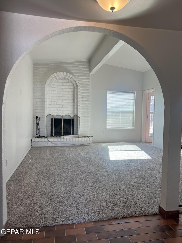 unfurnished living room with a brick fireplace, arched walkways, carpet, baseboards, and vaulted ceiling with beams