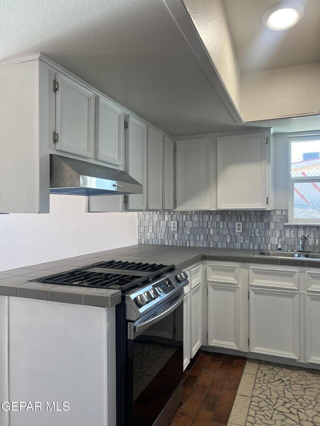 kitchen featuring stainless steel range with gas cooktop, decorative backsplash, under cabinet range hood, and white cabinets
