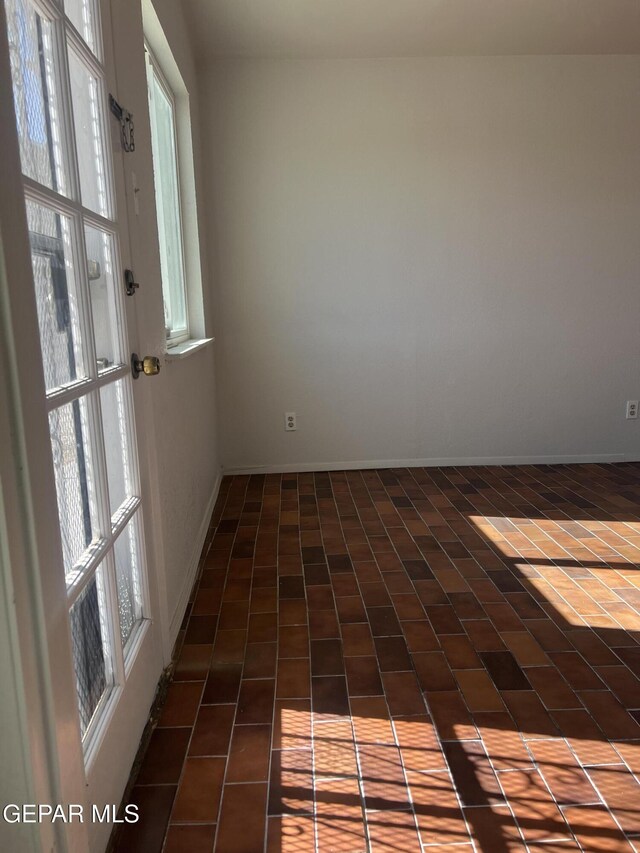 empty room with baseboards, plenty of natural light, and brick floor