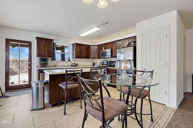 kitchen featuring dark brown cabinetry, visible vents, a kitchen island, appliances with stainless steel finishes, and light countertops