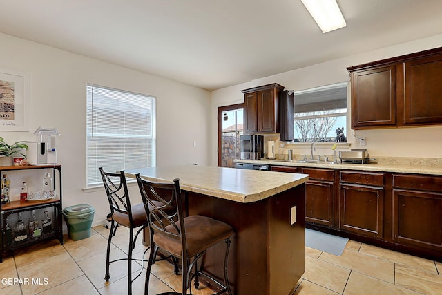 kitchen with light tile patterned flooring, a breakfast bar, a sink, light countertops, and a center island