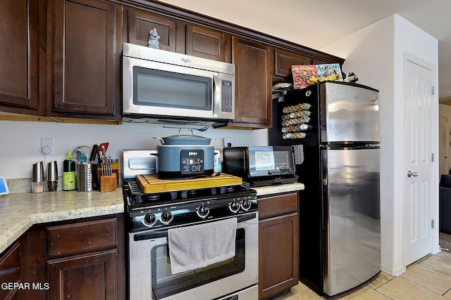 kitchen with light tile patterned floors, dark brown cabinetry, a toaster, light countertops, and appliances with stainless steel finishes