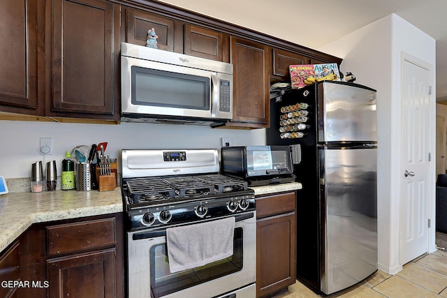 kitchen with stainless steel appliances, a toaster, dark brown cabinetry, and light tile patterned floors