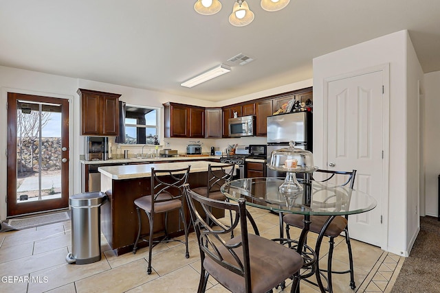 kitchen with light countertops, visible vents, appliances with stainless steel finishes, a kitchen island, and dark brown cabinets