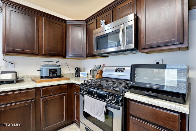 kitchen with dark brown cabinets, appliances with stainless steel finishes, and light stone countertops