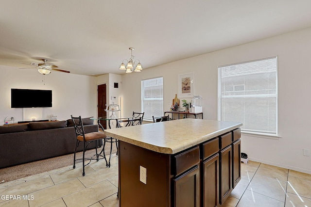 kitchen featuring a center island, light tile patterned floors, light countertops, dark brown cabinets, and ceiling fan with notable chandelier