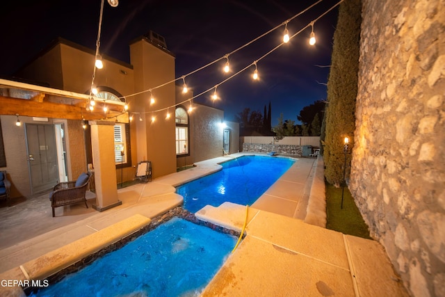 pool at night with a patio area, a fenced backyard, and a pool with connected hot tub