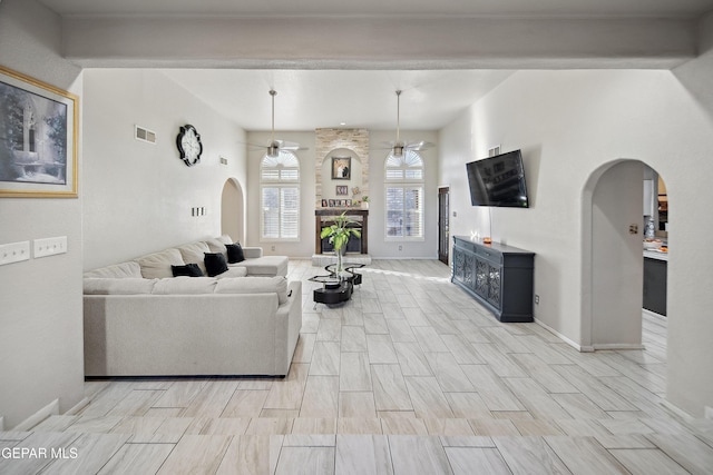 living room with arched walkways, wood finish floors, visible vents, a fireplace with raised hearth, and ceiling fan