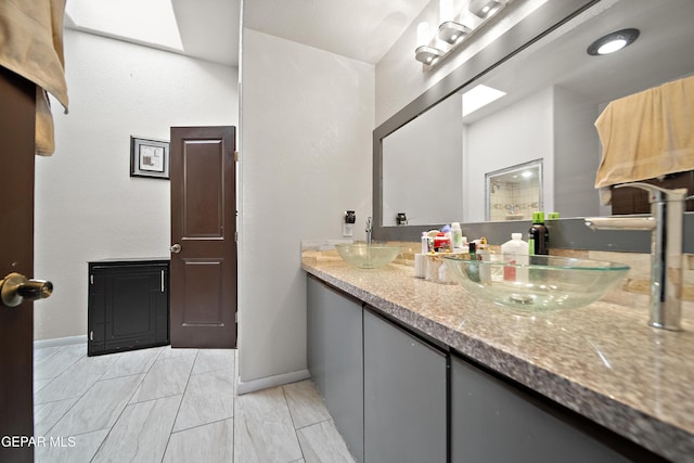 full bath featuring double vanity, a skylight, baseboards, and a sink