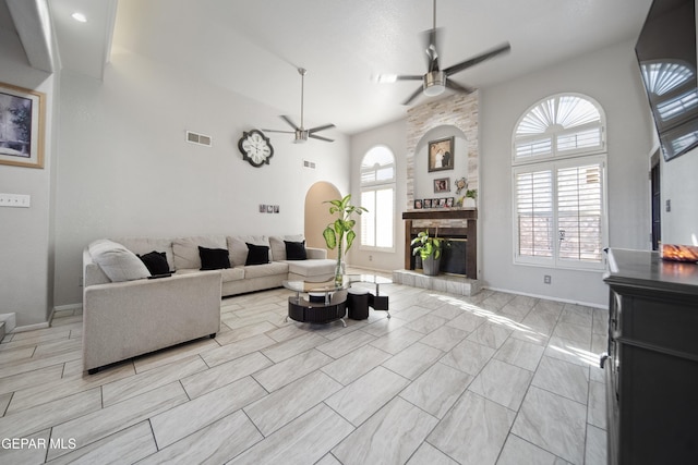 living room with a fireplace, visible vents, a high ceiling, a ceiling fan, and baseboards