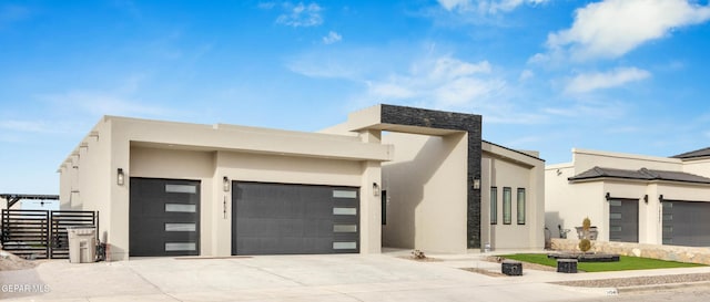 modern home with a garage, driveway, fence, and stucco siding