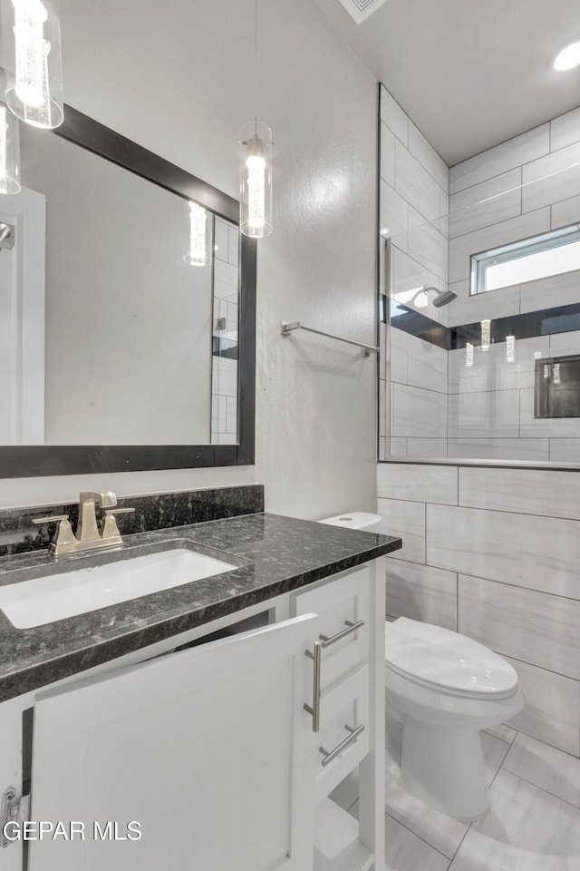 full bath featuring vanity, walk in shower, toilet, and tile walls