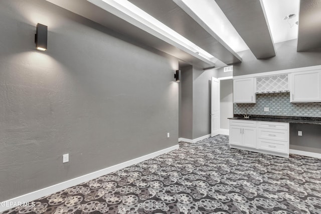 kitchen featuring dark countertops, backsplash, beam ceiling, and white cabinets