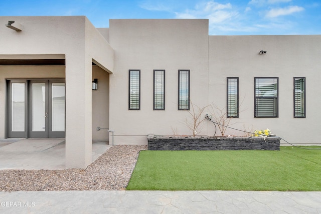 exterior space with stucco siding, a lawn, and french doors