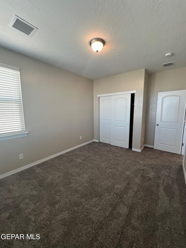 unfurnished bedroom featuring dark colored carpet, a closet, visible vents, and baseboards