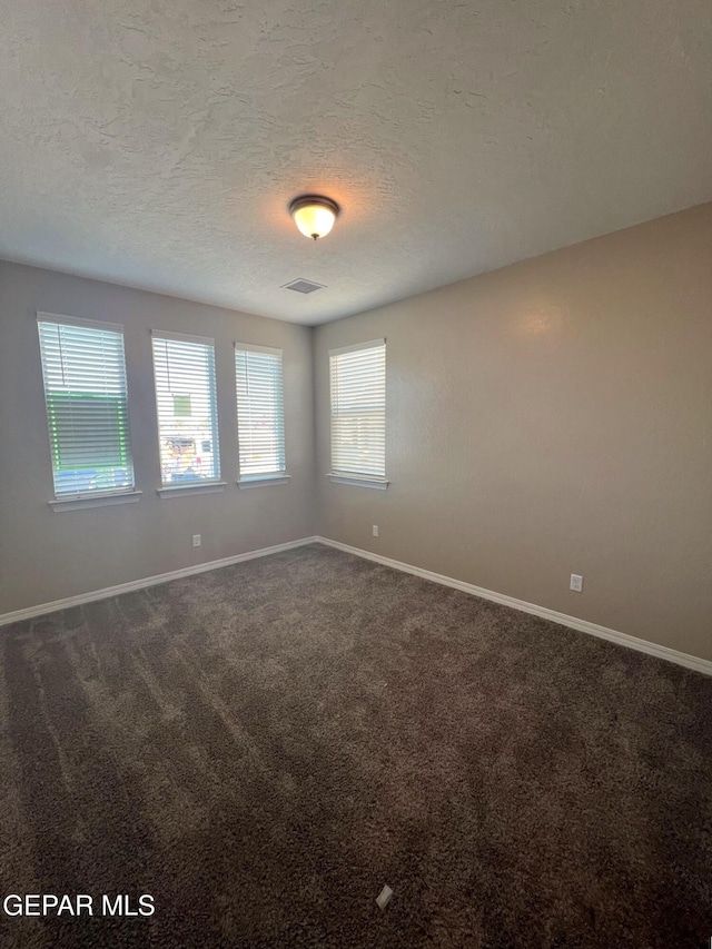 unfurnished room featuring baseboards, visible vents, dark carpet, and a textured ceiling