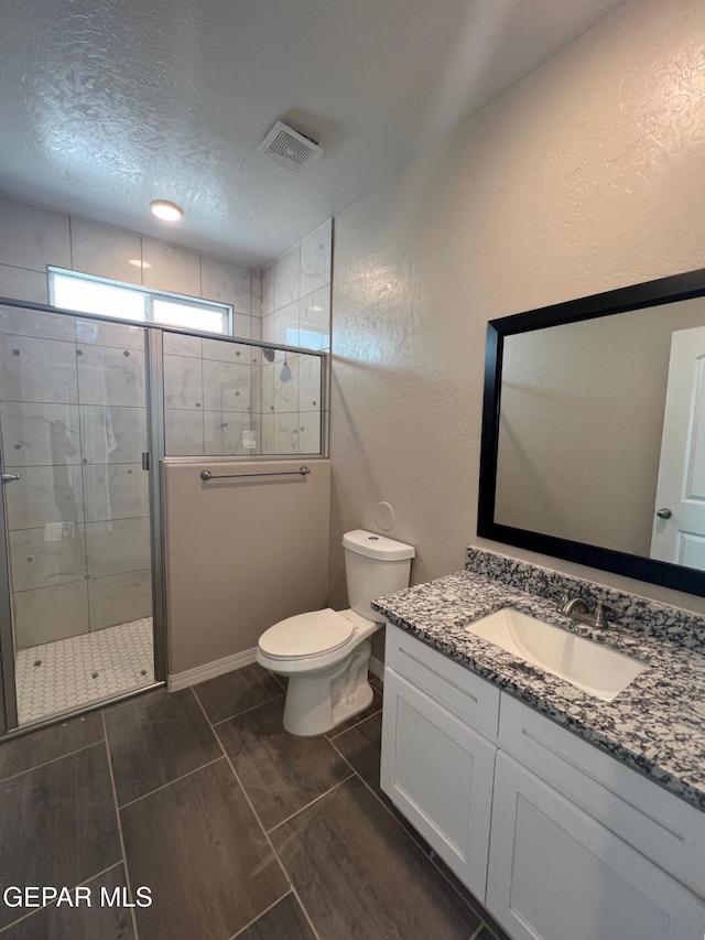 full bath with visible vents, toilet, vanity, a shower stall, and a textured ceiling