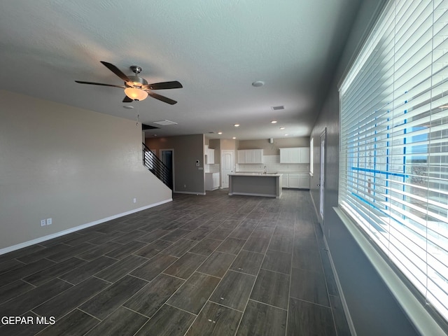 unfurnished living room with baseboards, ceiling fan, a textured ceiling, wood finish floors, and a sink