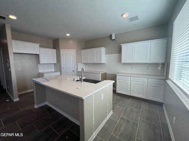 kitchen featuring a kitchen island with sink, a sink, visible vents, white cabinetry, and backsplash