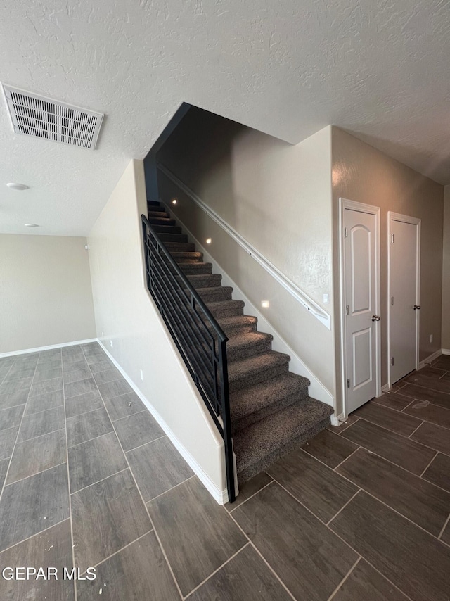 staircase featuring baseboards, visible vents, a textured ceiling, and wood finish floors