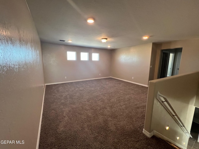 below grade area with dark carpet, visible vents, and baseboards