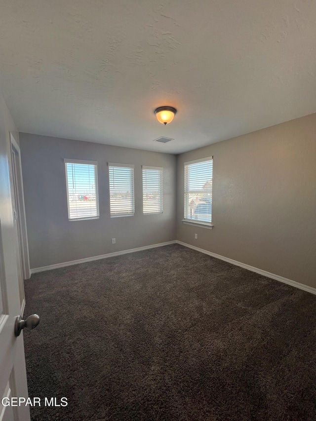 unfurnished room featuring baseboards, visible vents, and dark colored carpet