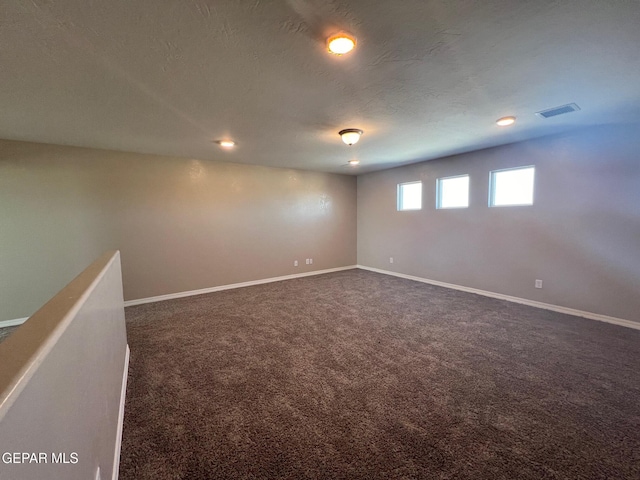 empty room featuring a textured ceiling, dark carpet, visible vents, and baseboards